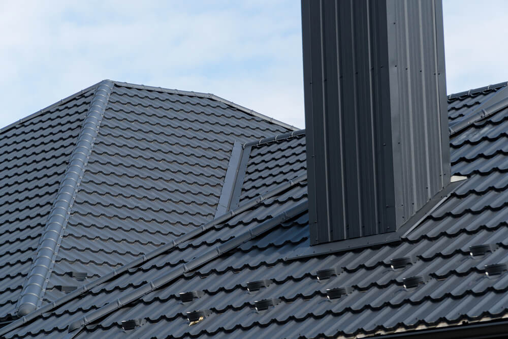 Modern black metal roofing with chimney against blue sky. Durable and stylish roof solution.