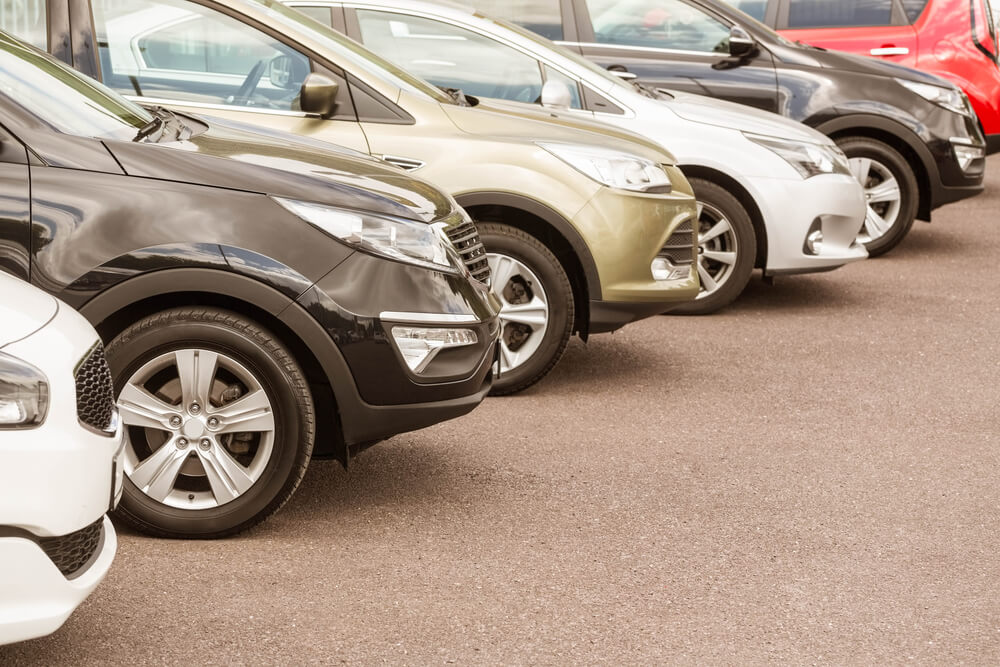 Row of parked cars in a lot showcasing various colors and models on a sunny day.