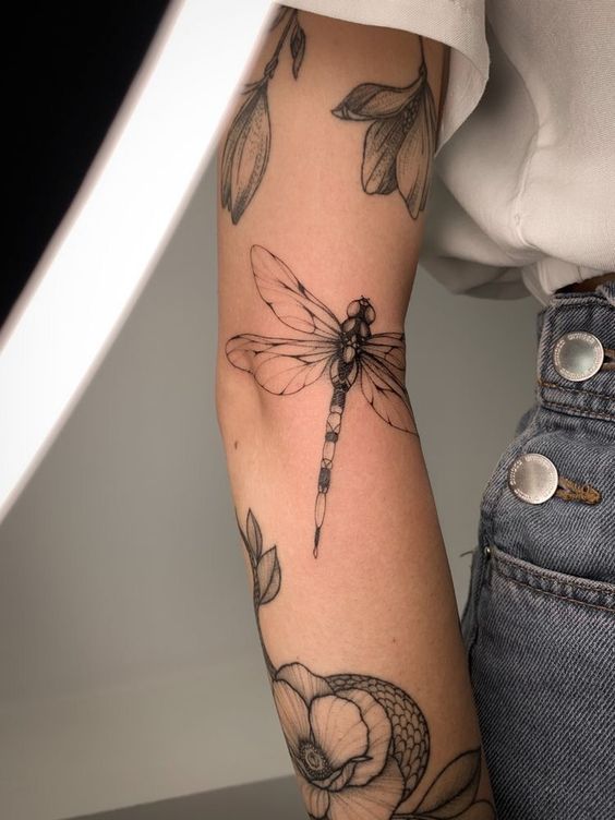 Detailed dragonfly and floral tattoos on a person's inner arm, embodying intricate and artistic design.