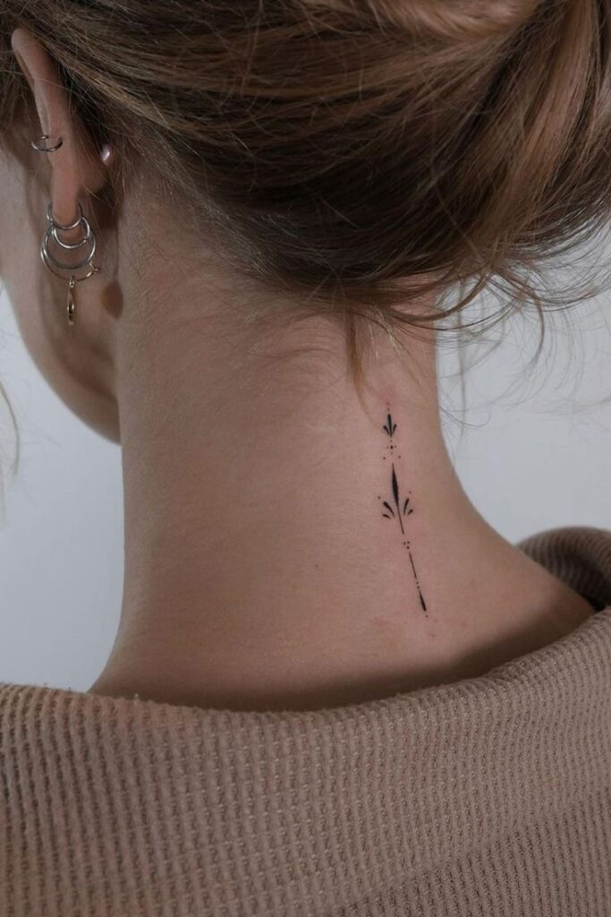 Minimalist neck tattoo with geometric design below ear, styled with hoop earrings and hair in bun.