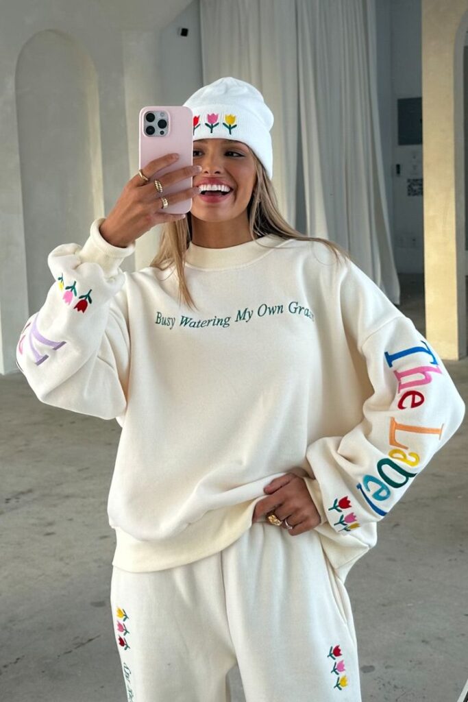 Smiling woman in floral tracksuit and beanie taking a selfie indoors. Cozy and stylish athleisure outfit.