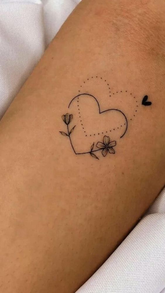 Minimalist heart tattoo with flowers on arm, featuring dotted lines and small floral details.