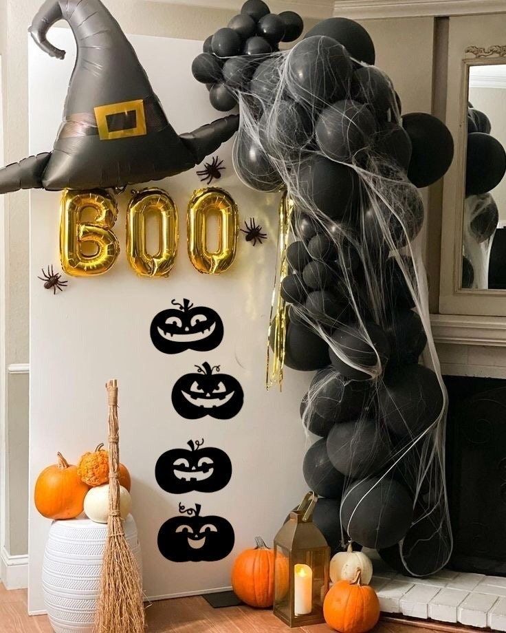 Spooky Halloween decor with black balloons, gold BOO, pumpkins, witch hat, and spider webs by a fireplace.