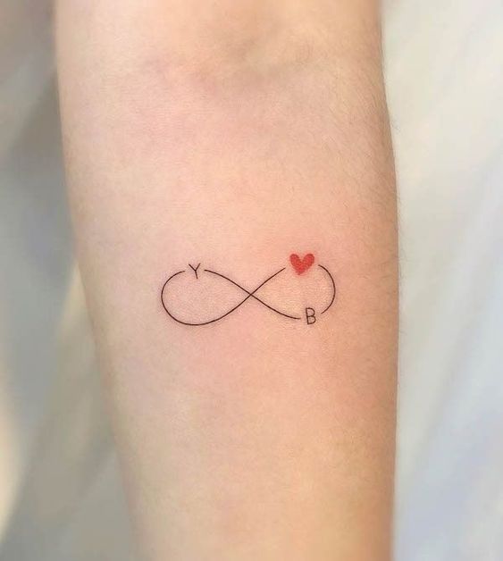 Infinity tattoo on arm with letters Y and B, and a red heart symbol, signifying eternal love.