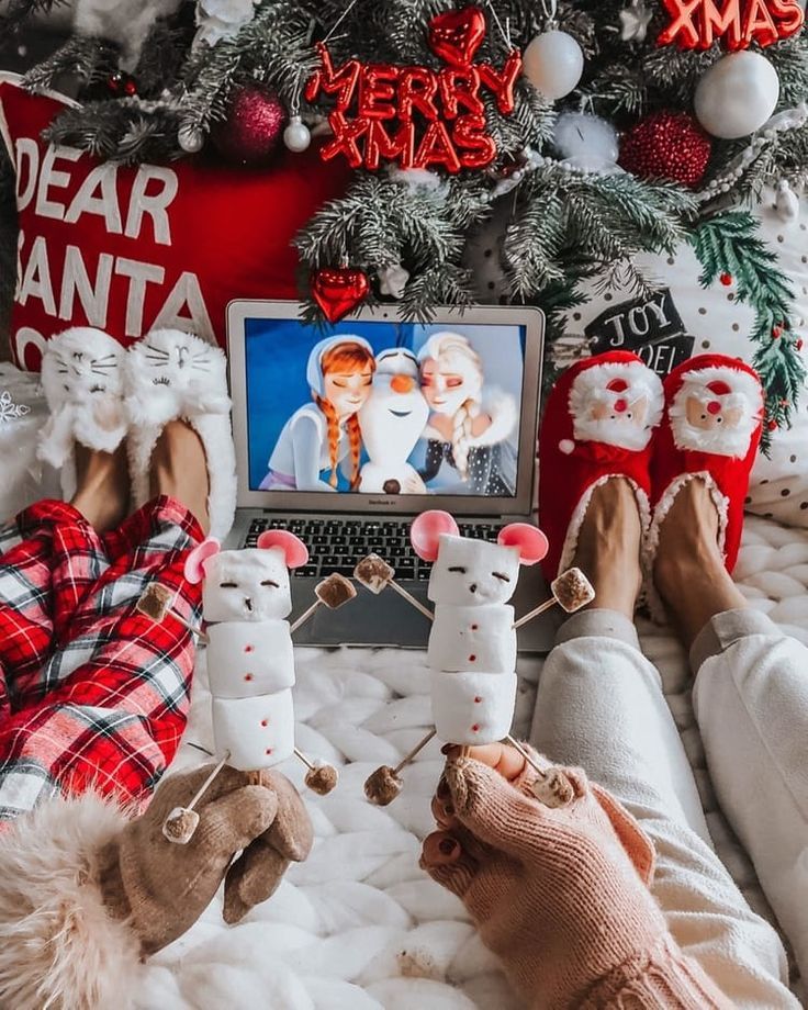 Cozy Christmas scene with festive slippers, marshmallow snowmen, and a holiday laptop movie under the decorated tree.