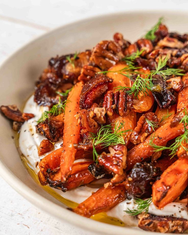 Roasted carrots with pecans, dates, and fresh dill on creamy yogurt sauce in a bowl.