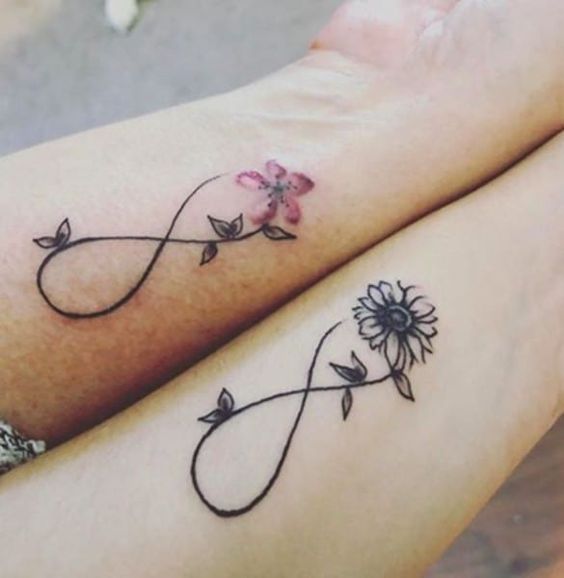 Infinity symbol tattoos with floral designs on arms, featuring a pink flower and a black sunflower.