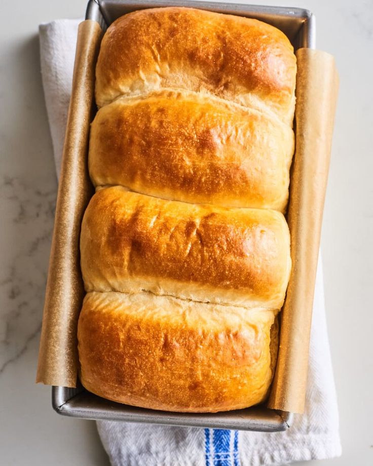 Freshly baked golden brown bread loaf in a pan on a white towel. Perfect for homemade baking enthusiasts.