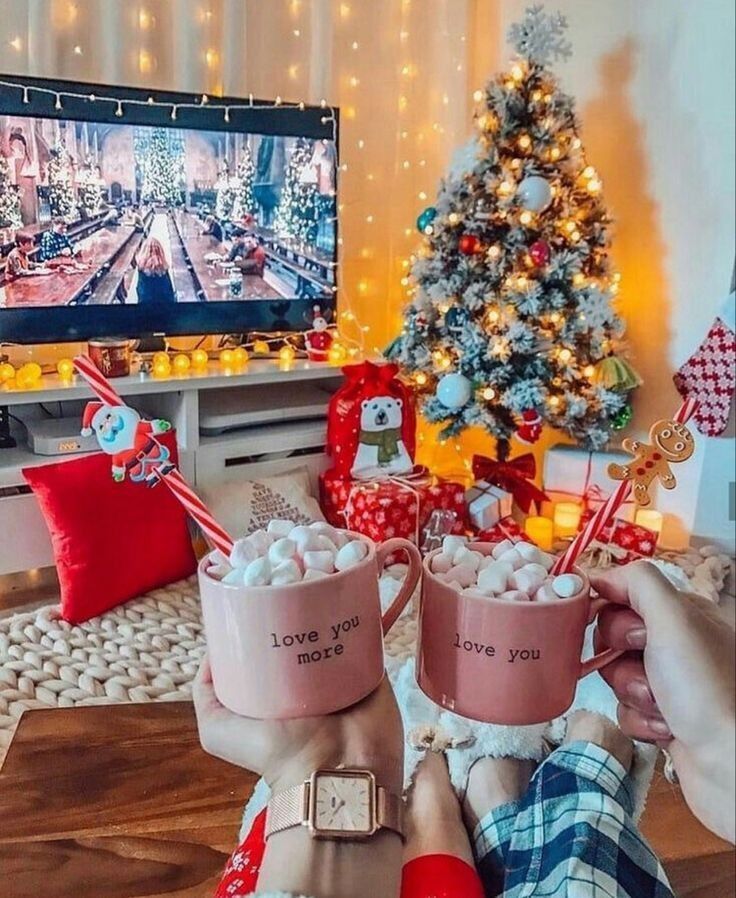 Cozy Christmas setting with hot cocoa, decorated tree, gifts, and festive movie on TV.