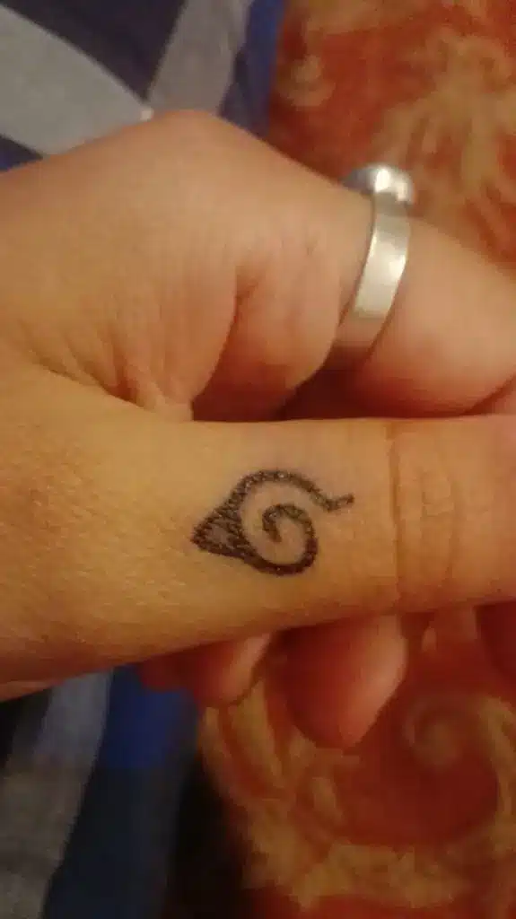 Konoha leaf 1 Close-up of hand with small spiral finger tattoo next to a simple silver ring on thumb, warm patterned background. | Sky Rye Design Close-up of hand with small spiral finger tattoo next to a simple silver ring on thumb, warm patterned background.