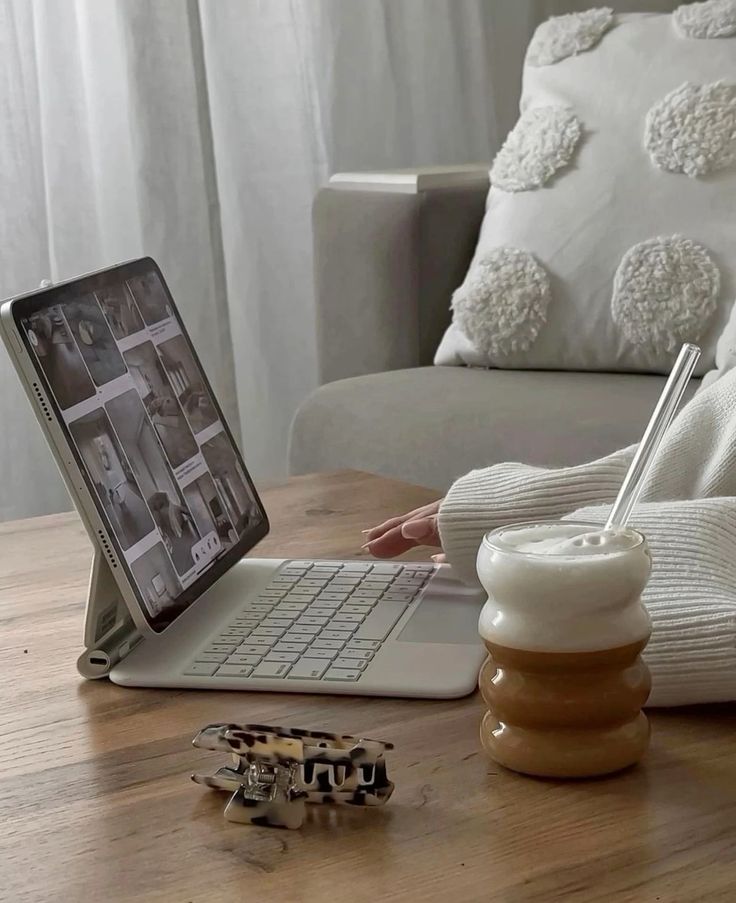 Person using tablet with keyboard on table, next to a frothy coffee and a hair clip in a cozy home setting.