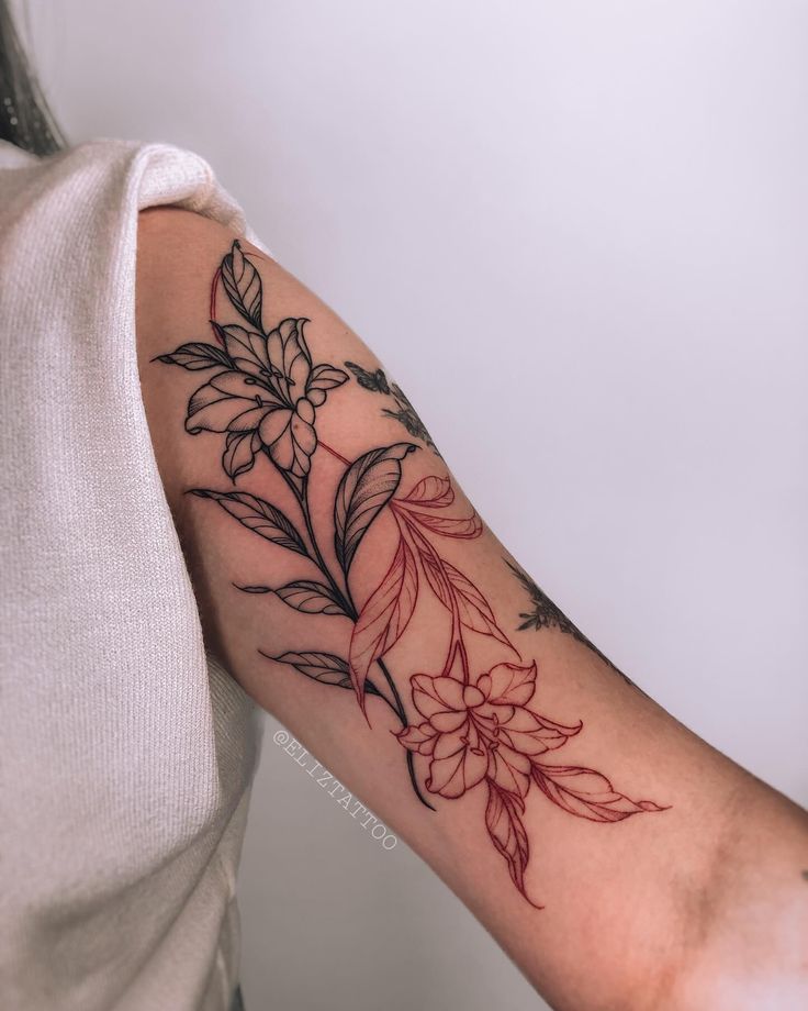 Elegant floral tattoo with intricate black and red linework on upper arm, showcasing detailed leaves and flowers.