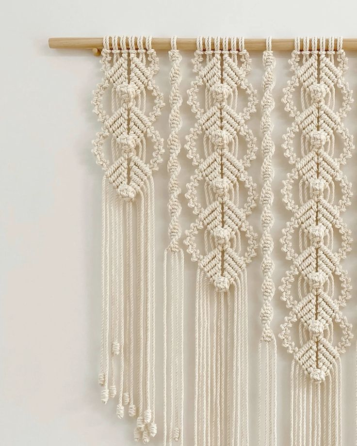 Intricate macramé wall hanging with detailed patterns and fringes, crafted with beige cord on a wooden dowel.