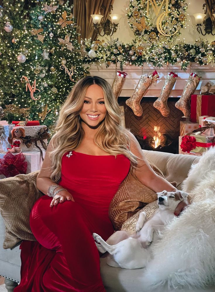 Woman in red dress sitting on a couch with Christmas decorations, stockings, and a fireplace in the background.