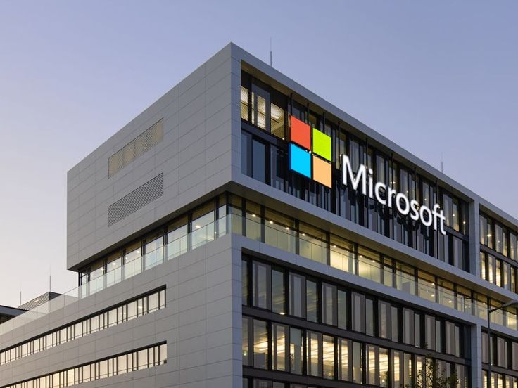 Modern Microsoft office building with logo, featuring large glass windows and sleek architecture against a clear sky.