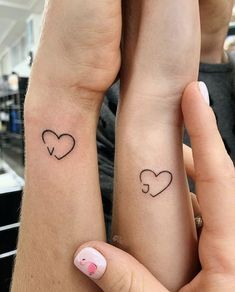 Minimalist heart tattoos on two wrists, symbolizing a shared connection and love in a modern style.