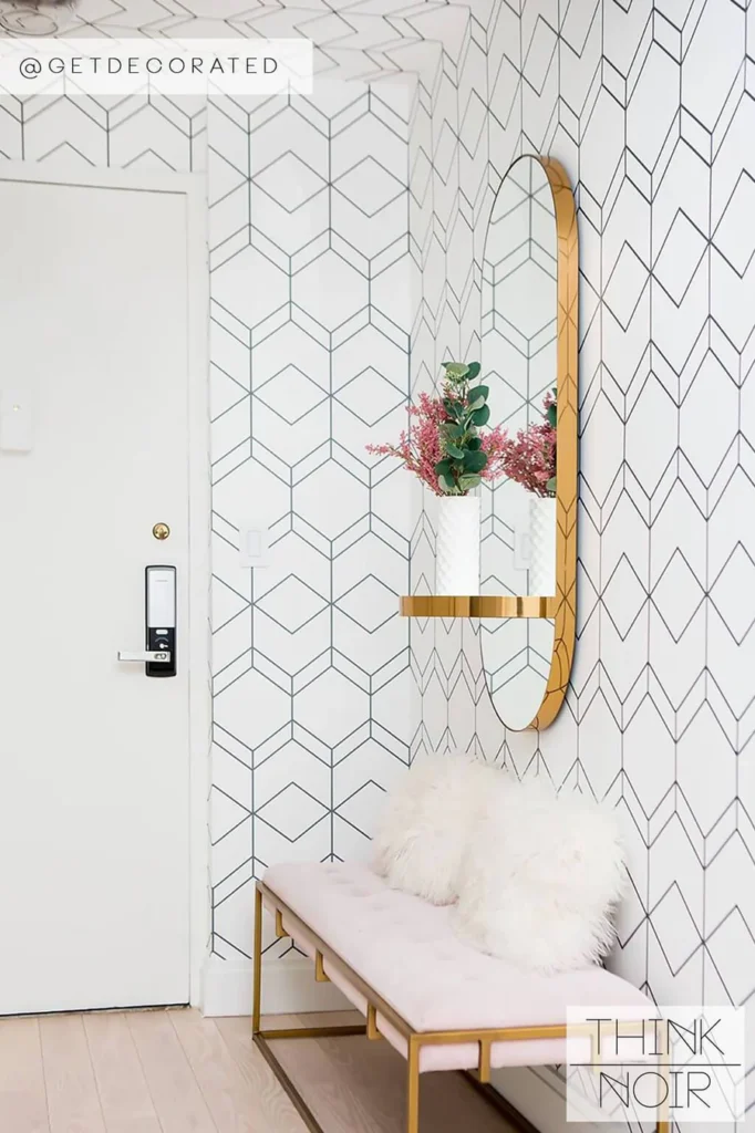 Modern entryway with geometric wallpaper, round mirror, gold shelf, and cozy bench with white pillows.