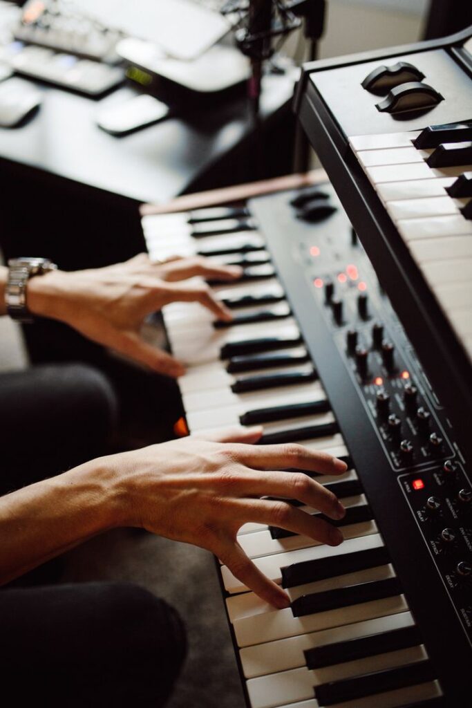 Hands playing on a synthesizer keyboard in a music studio.