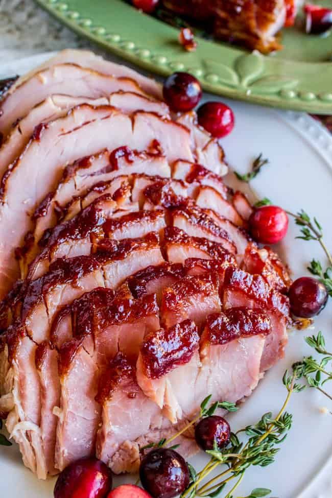 Sliced glazed ham garnished with fresh cranberries and thyme on a white plate, perfect for a festive holiday meal.