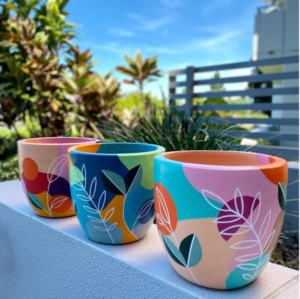 Colorful hand-painted plant pots with abstract leaf designs outdoors against a vibrant blue sky.