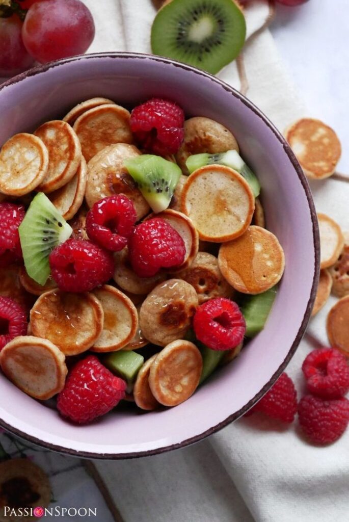 Bowl of mini pancakes topped with fresh raspberries and kiwi slices, creating a vibrant and delicious breakfast.