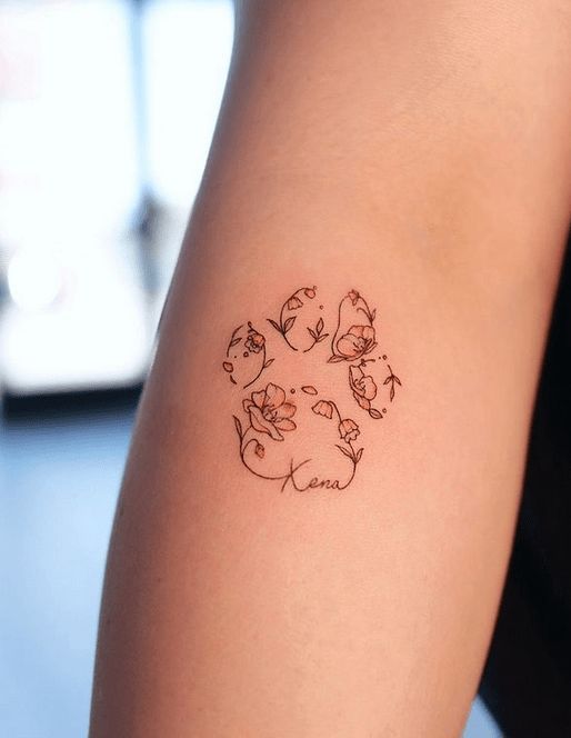 Minimalist floral tattoo on forearm, featuring delicate flowers and leaves with a personalized name design.