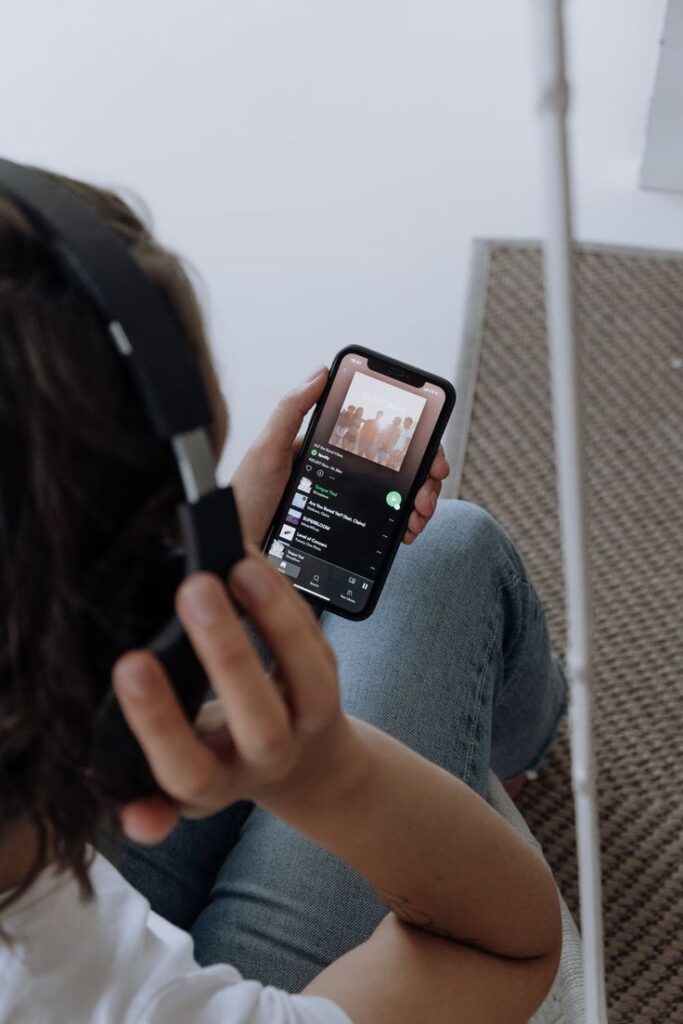 Person with headphones listening to music on a smartphone, displaying a playlist screen.