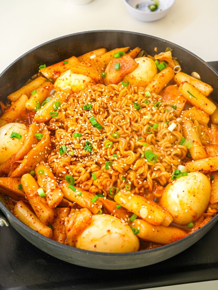 Spicy Korean tteokbokki with ramen, boiled eggs, and green onions in a sizzling pan. Perfect for savory food lovers.