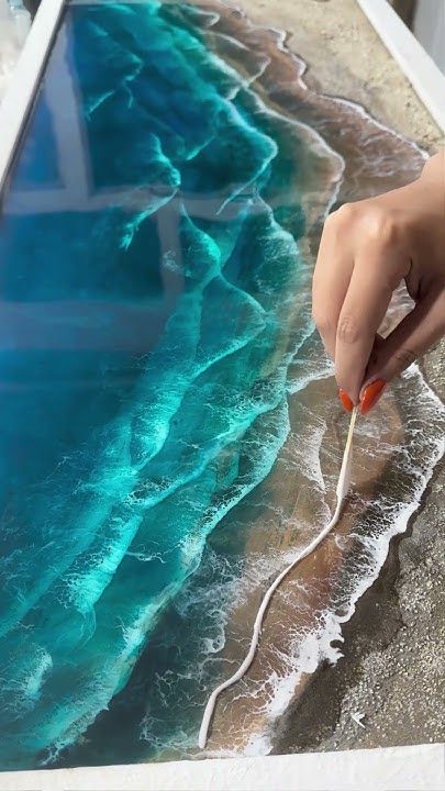 Hand crafting realistic ocean waves in resin art on a table, showcasing detailed textures and vibrant blue hues.