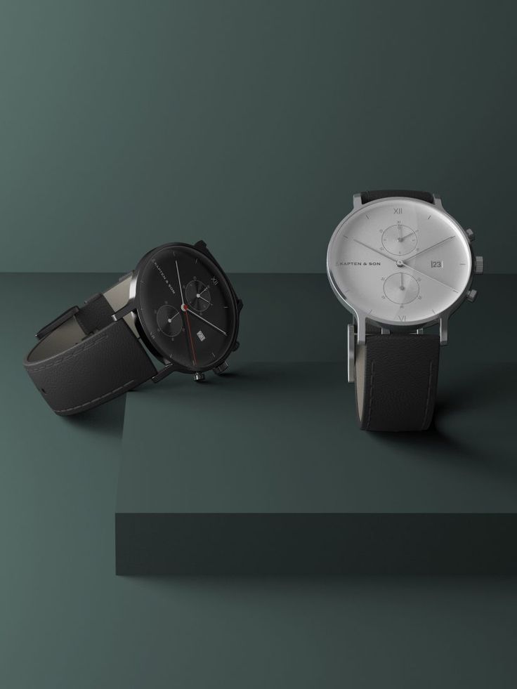 Two sleek men's watches with leather straps displayed on a dark green surface, featuring a modern minimalist design.