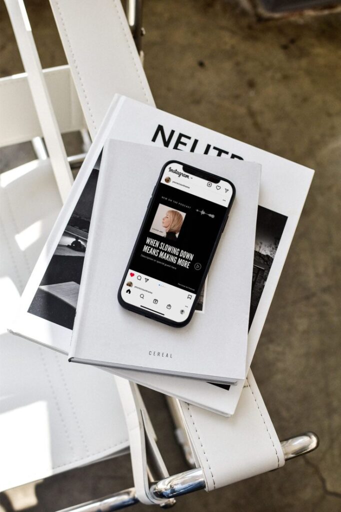 Smartphone on stacked magazines featuring Instagram post about slowing down, atop a white chair.