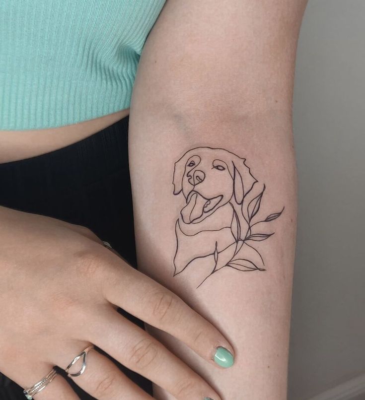 Minimalist dog tattoo design on forearm with leafy accents, showcasing simple line art style.