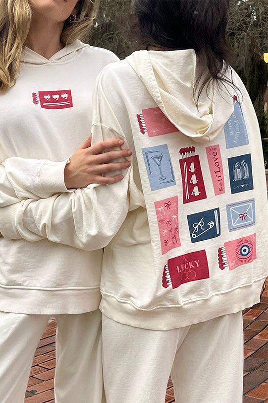 Two individuals wearing white graphic hoodies with unique designs, outdoors on a brick path.