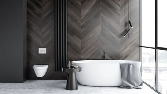 Modern bathroom with sleek bathtub, dark chevron wall tiles, wall-mounted toilet, and large windows for natural light.