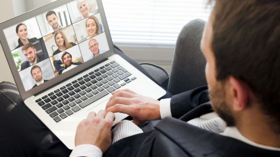 Man in a suit participates in a video conference on laptop with multiple colleagues on screen, remote work concept.