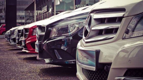 Row of luxury cars parked in a dealership lot, showcasing sleek designs and varied colors.