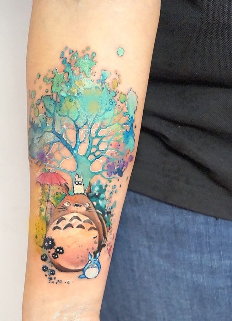 Watercolor Anime Tattoos 2 Watercolor Totoro forearm tattoo with blue tree, soot sprites, red umbrella and small Totoros in vibrant splatter-style ink. | Sky Rye Design Watercolor Totoro forearm tattoo with blue tree, soot sprites, red umbrella and small Totoros in vibrant splatter-style ink.