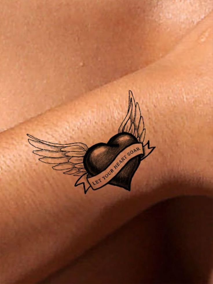 Heart with wings tattoo on skin, featuring the phrase Let Your Heart Soar in banner.