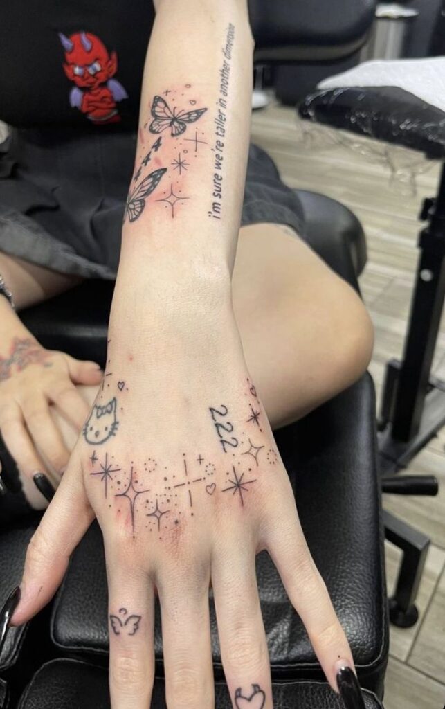 Hand and forearm with butterfly, stars, and 222 tattoos, seated in a tattoo parlor.