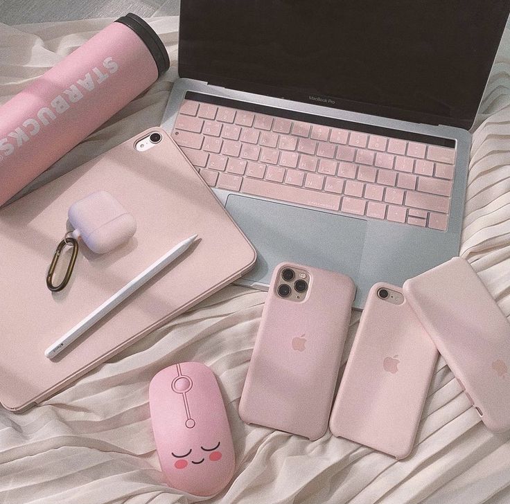 Pink-themed tech accessories on a bed: MacBook, phones, tablet, mouse, and Starbucks tumbler.