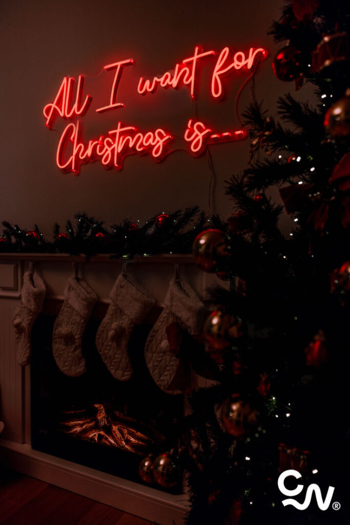 Cozy Christmas scene with neon sign, stockings by the fireplace, and decorated tree.