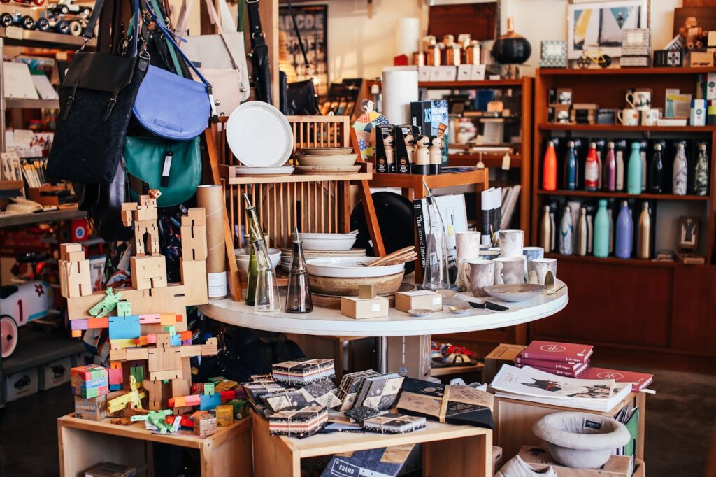 Eclectic store display with handbags, wooden toys, dishware, bottles, and home decor items on shelves and tables.