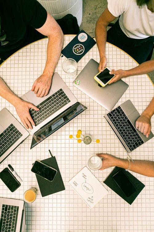 Teamwork at a round table with laptops and smartphones, collaborating and sharing ideas in a modern office setting.