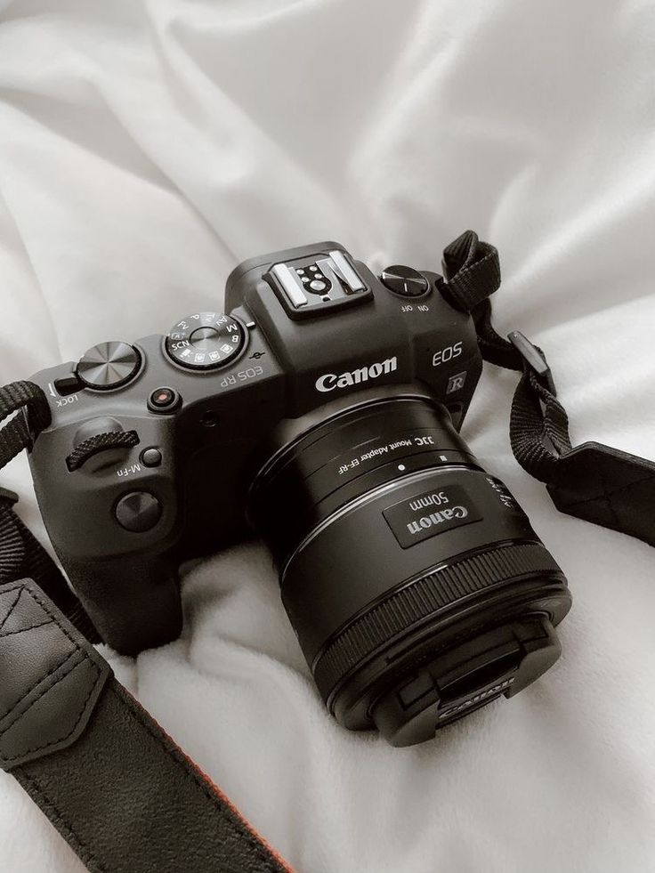 Canon EOS camera with 50mm lens on a soft white fabric background, ideal for photography enthusiasts.