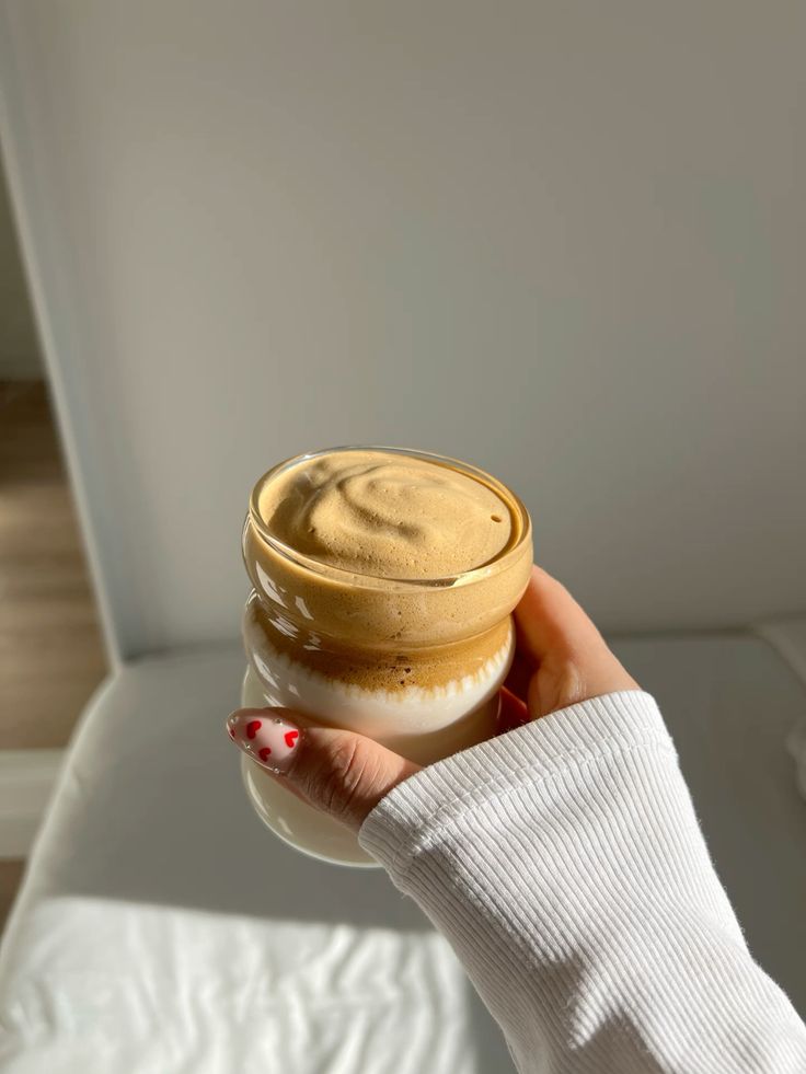 Hand holding a creamy whipped coffee in a transparent glass jar, showcasing a trendy Dalgona coffee drink.