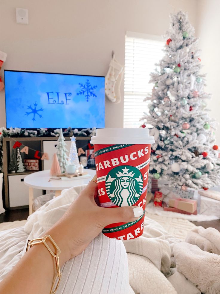 Cozy Christmas setup with a Starbucks holiday cup, a frosted tree, and Elf on TV. Perfect holiday vibes!