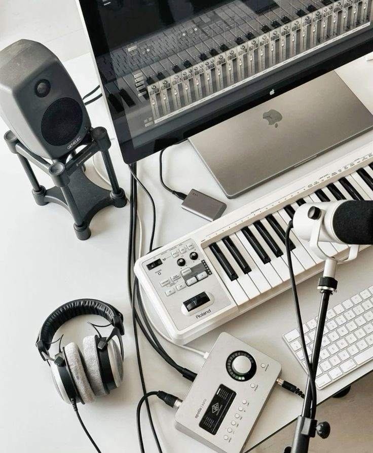 Modern music production setup with a computer, keyboard, microphone, headphones, and speakers on a white desk.