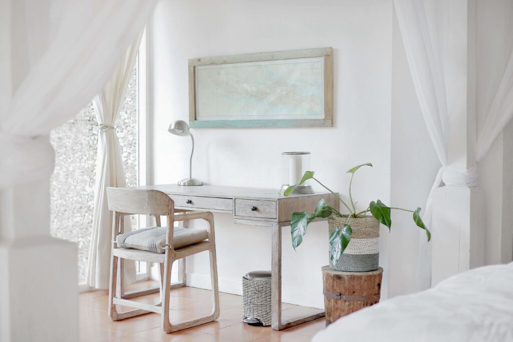 Minimalist home office with wooden desk, chair, plant, and framed map on white wall. Bright and airy natural light.