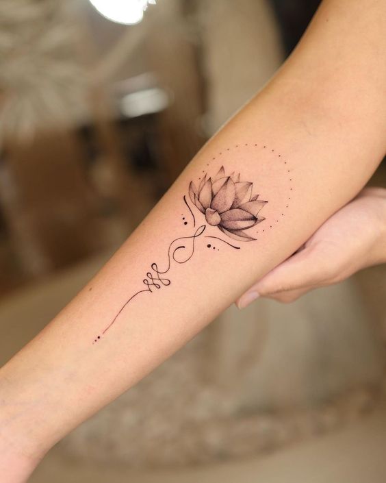 Minimalist lotus flower tattoo on forearm, featuring delicate line work and dot detailing.