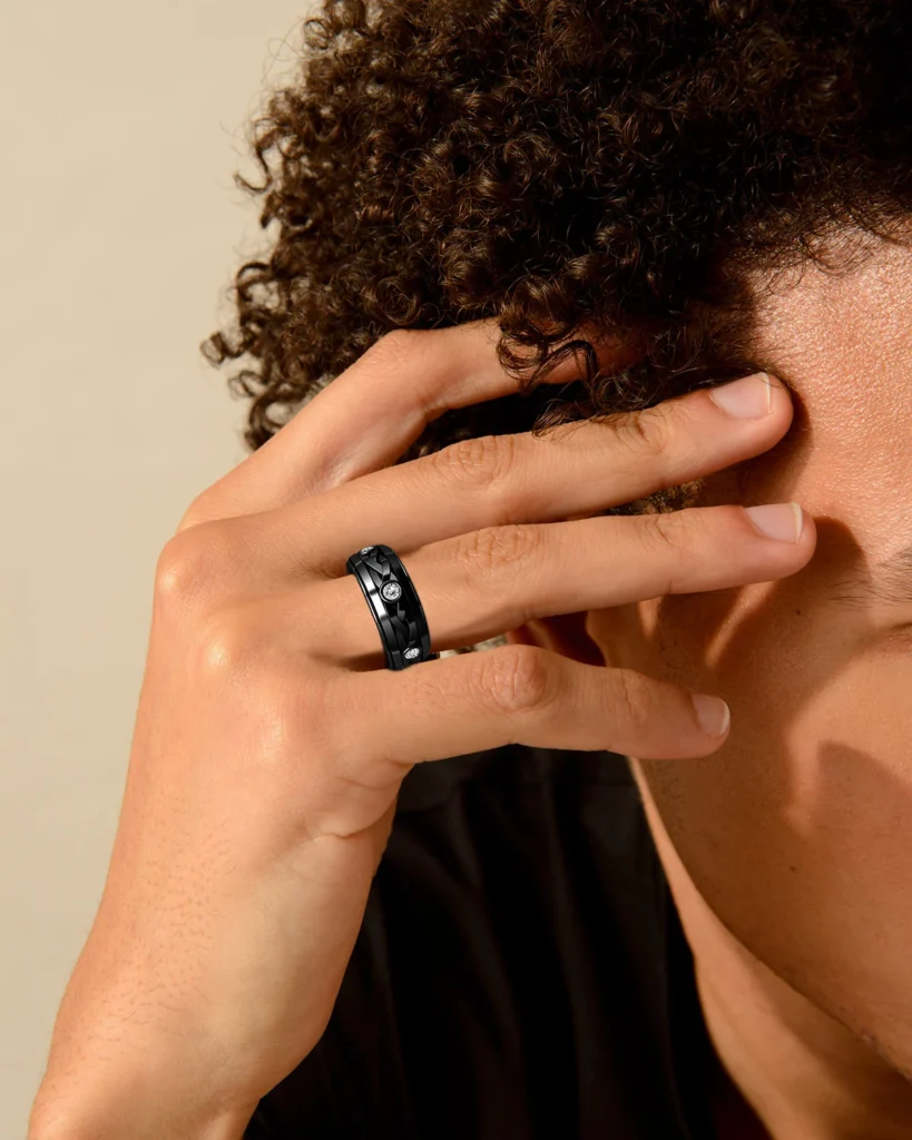 Man wearing a stylish black ring with diamonds, touching his curly hair.